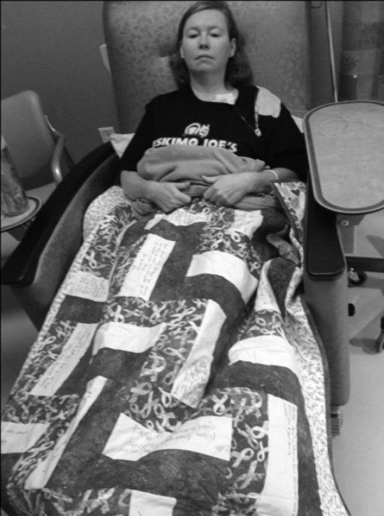 Person resting in a hospital chair covered with a patterned quilt, appearing calm and comfortable.